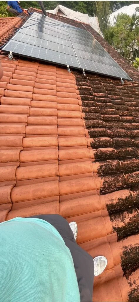 Cleaned and stained areas of clay roof tiles during cleaning beside a solar installation
