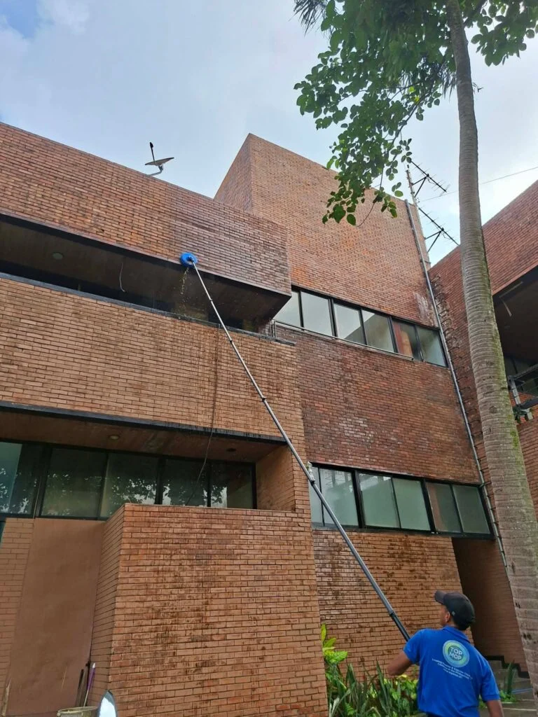 TopMop crew using a pole-mounted rotating cleaner on elevated brick walls